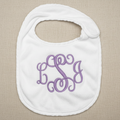 A white baby bib with a purple monogram embroidery featuring the letters 'B', 'S', and 'G' in a cursive script, displayed on a white fabric background.