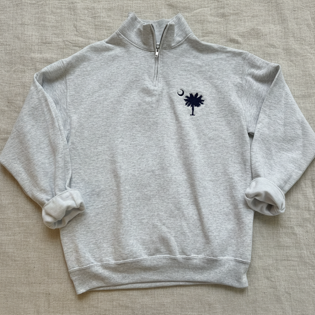 A light heather gray quarter-zip sweatshirt featuring the navy blue South Carolina Palmet and Spear logo with a crescent moon on the left chest, displayed flat against a white background.