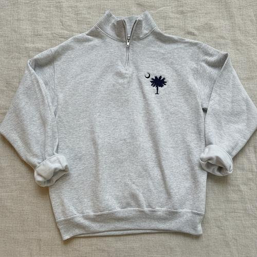 A light heather gray quarter-zip sweatshirt featuring the navy blue South Carolina Palmet and Spear logo with a crescent moon on the left chest, displayed flat against a white background.