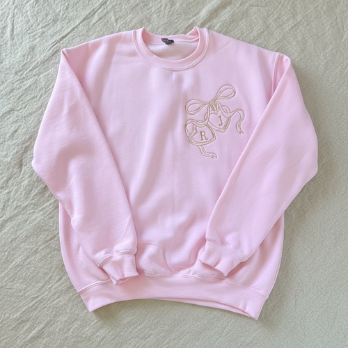A light pink crewneck sweatshirt featuring a gold line-art graphic of three hanging bells on the left chest, laid flat against a white background.