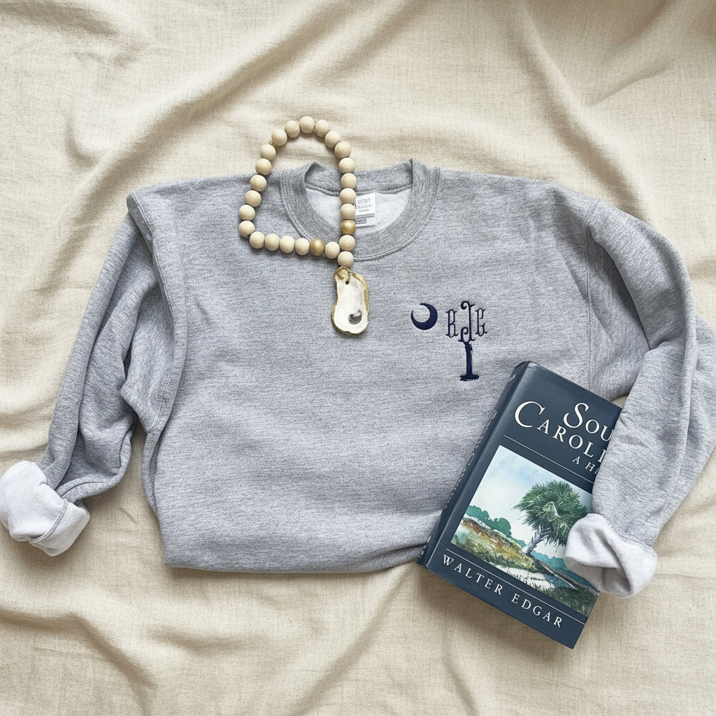 A heather gray crewneck sweatshirt with a navy blue palmetto tree with a monogram as the top of the tree  
