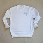 A white crewneck sweatshirt with a light blue graphic on the left chest depicting a crescent moon and a stylized tree, laid flat against a white background.