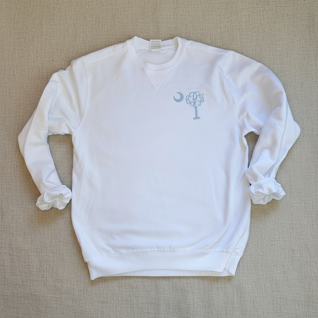 A white crewneck sweatshirt with a light blue graphic on the left chest depicting a crescent moon and a stylized tree, laid flat against a white background.