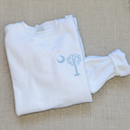 A folded white baby long-sleeve shirt with a matching footed sleeper, featuring a light blue embroidered monogram design on the chest.