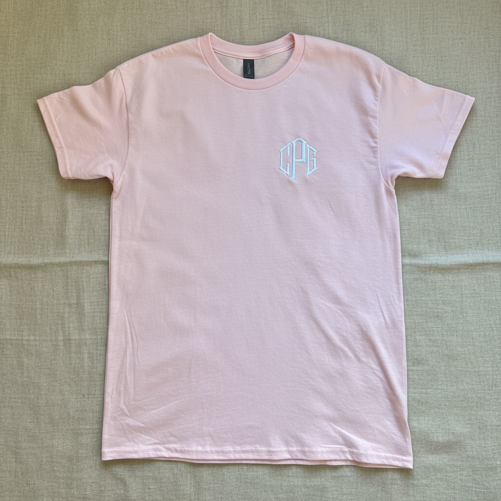 A light pink short-sleeve crewneck t-shirt with a small light blue geometric monogram logo on the left chest, laid flat against a white background.